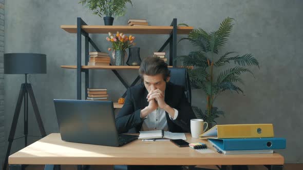A Young Attractive Businessman Works on a Laptop for a Long Time and Wearily Rubs His Eyes While