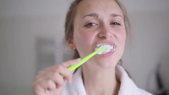 Closeup of Brunette Young Woman with Brown Eyes Brushing Teeth in Slow Motion Smiling Looking at
