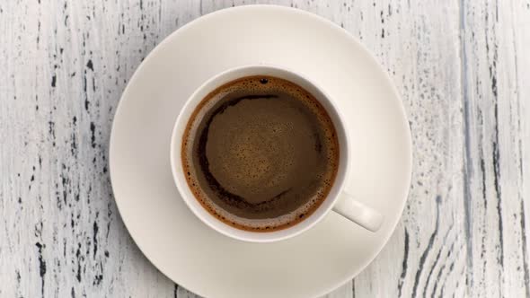 Coffee Foam Swirls in White Cup with Black Coffee. Shabby White Wooden Background. Top Down View