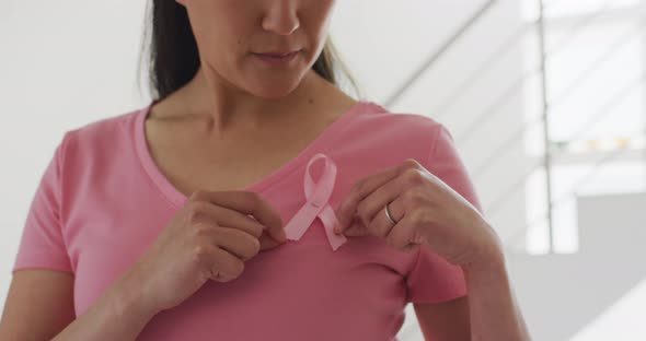 Happy asian woman in pink tshirt showing pink ribbon at home