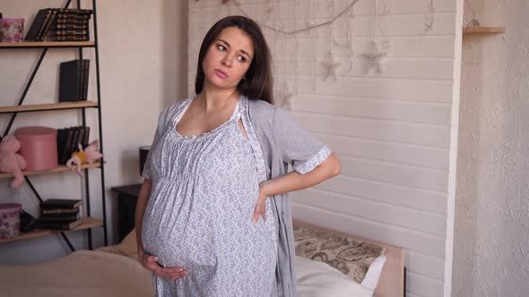 Sad Pregnant Woman with Stomach Pain or Backaches in Pyjamas in the Bedroom