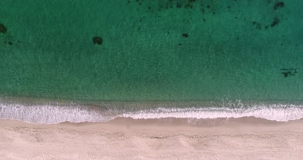 Static top down view of tropical beach, foamy ocean waves washing sand. Waves hitting sand beach