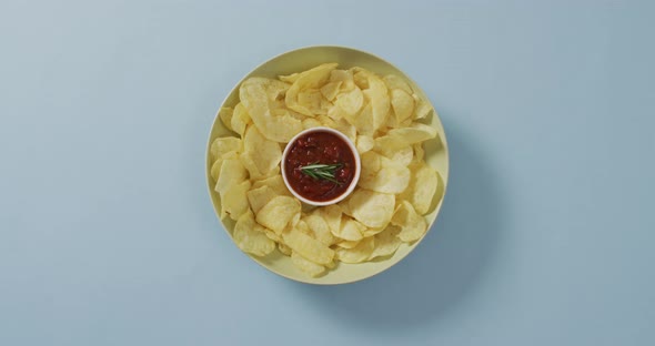 Close up of potato chips in a bowl with sauce on blue surface