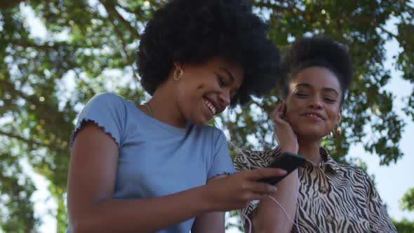 Two mixed race women listening music in park