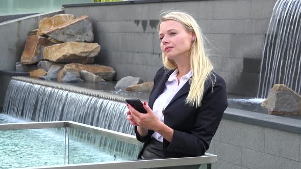 A Young Beautiful Businesswoman Works on a Smartphone in an Urban Area - Artificial Waterfalls