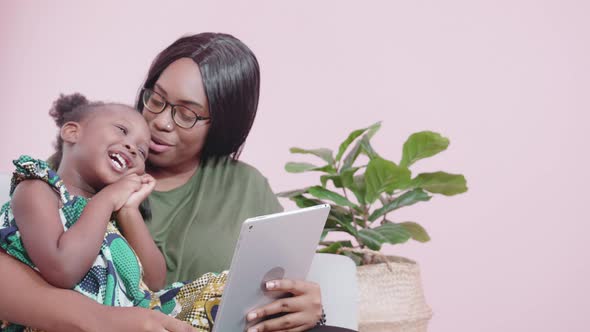 Young african mother and daughter learning on tablet computer on sofa at home.