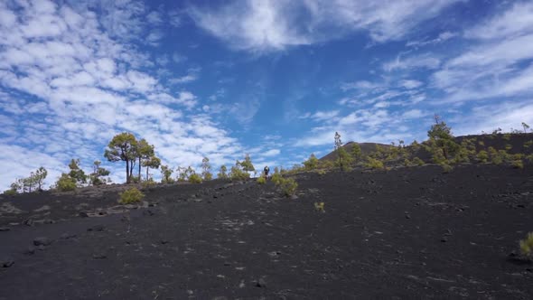 A hiker in the distant hikes up a volcano beneath a beautiful cloudy sky