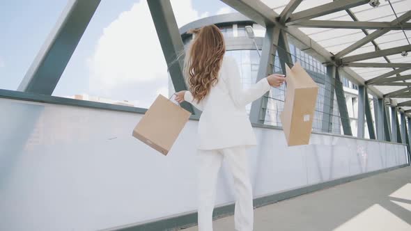 Sexy smiling woman in white suit walks with shoping bags in the city urban street. Steadicam stabili