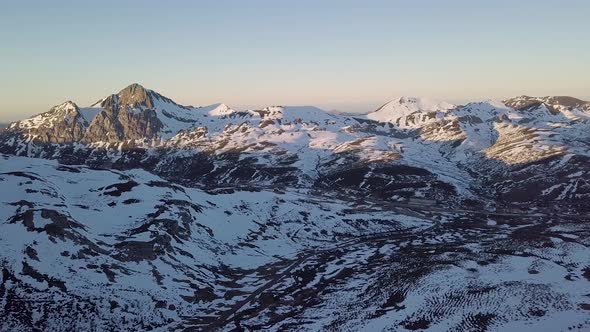 Aerial View Zooming Out of Vast Snowy Mountainous Landscape During Golden Hour