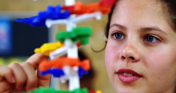 Schoolgirl experimenting molecule model in laboratory at school