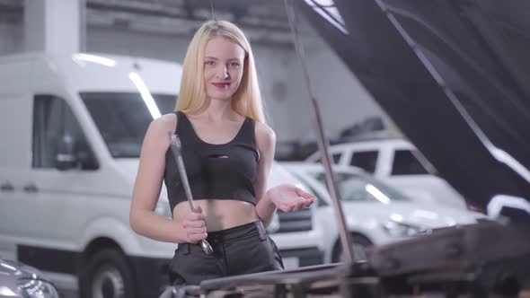 Portrait of Sexy Blond Caucasian Woman Standing Next To Open Car Hood with Adjustable Wrench 