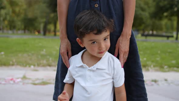 Cute Funny Little Boy Standing By Mom Outdoors