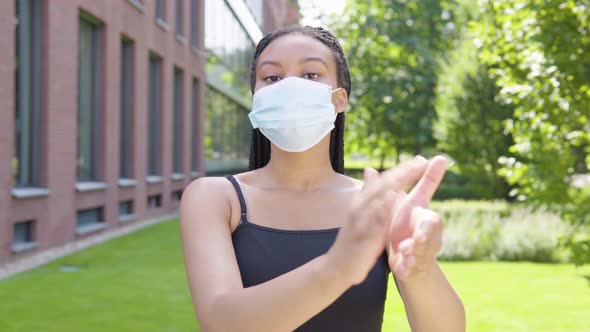 A Young Black Woman in a Face Mask Applauds To the Camera - an Office Building