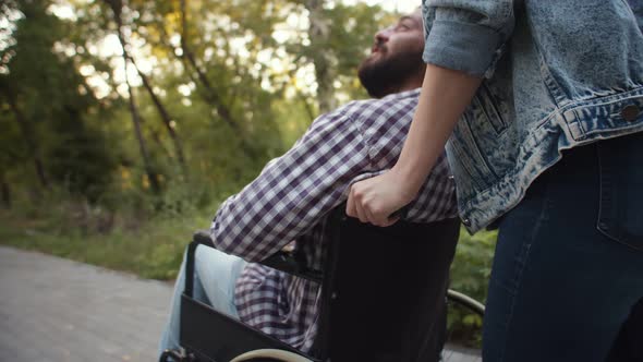 Woman Rolls Disabled Person in Wheelchair Through Park Side Down View