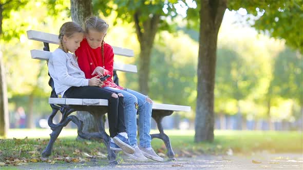 Little Adorable Girls with Smartphone in Fall. Kids Having Fun at Warm Sunny Autumn Day Outdoors