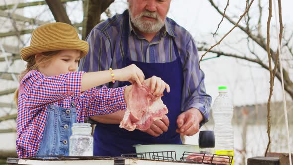 Granddaughter Helps Grandfather Cook Barbecue and Puts the Meat on the Grill