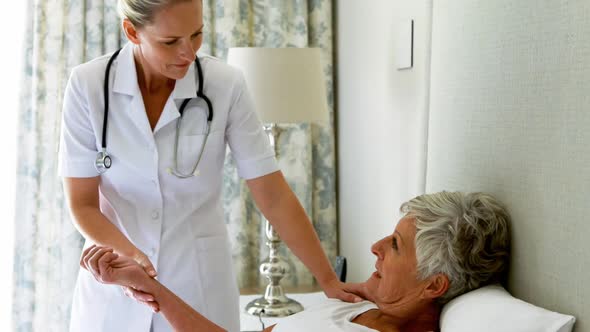 Female doctor checking senior woman pulse during check up in bedroom