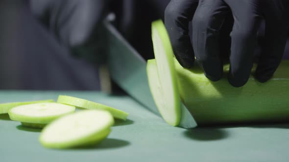 Cook's Hands in Black Gloves Slicing Zucchini Close Up Selective Focus