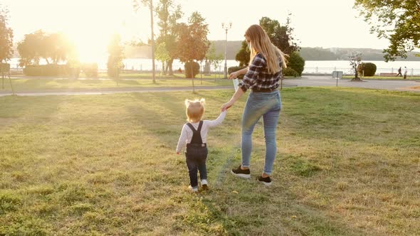 Young Mother Walks with Little Daughter in a Public Park