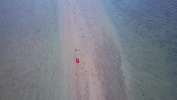 Aerial view of young brunette woman in red dress walking on sandbar in Asia - camera tracking backwa