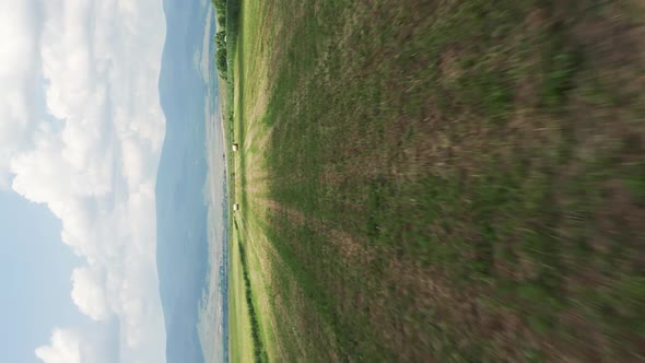 Vertical video: low aerial shot over harvested farmland, hay bales in field