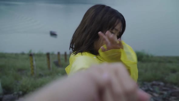 Young Asian woman feeling happy playing rain while wearing raincoat standing near lake.