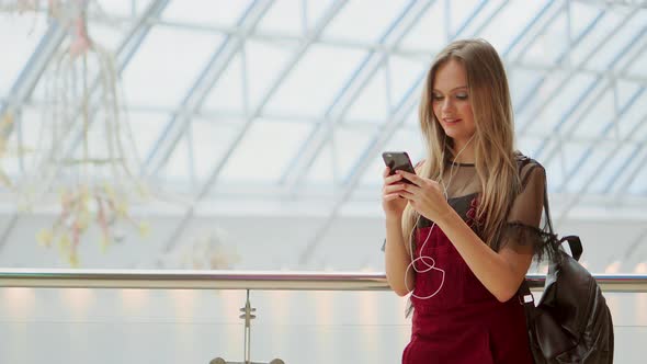 Happy Teenage Girl Holding Bags with Purchases, Smiling While Looking at Phone in Shopping Center