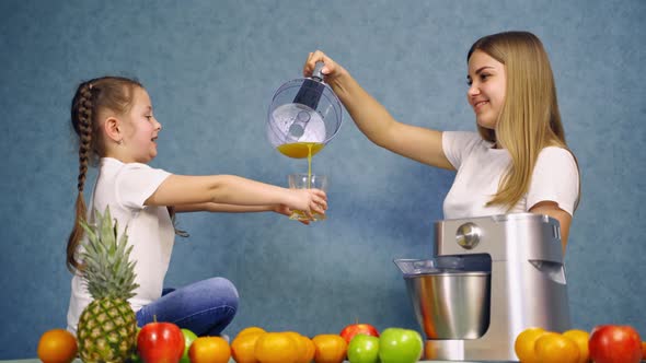 Happy family drinking juice. Smiling girl sitting on the table with fruits and juice