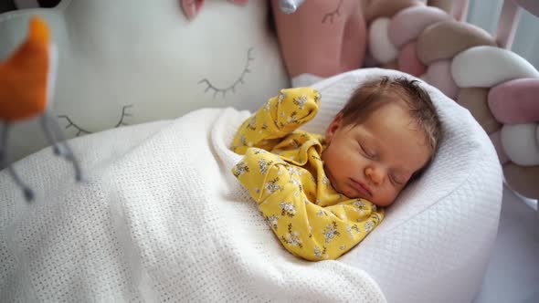 Newborn in a Yellow Jumpsuit Lies in a Retainer of the Child in a Crib