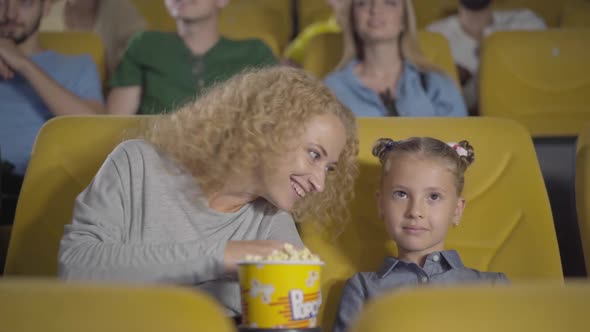 Embarrassed Caucasian Mother Closing Daughter's Eyes in Cinema, Portrait of Relaxed Parent and Child