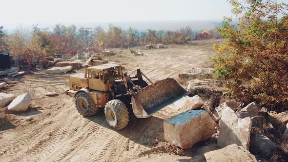 professional yellow bulldozer with a bucket is working in the quarry with stones