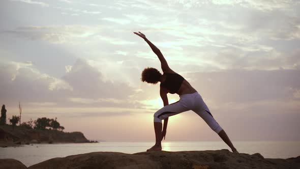 Sportive African American Girl Standing in Yoga Asana on Rocks By the Sea with Facing Sun