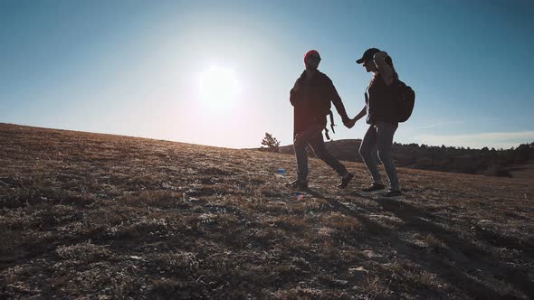 Low Angle Couple Walking on Field of Mown Wheat on Hilly Terrain at Sunset Full Shot