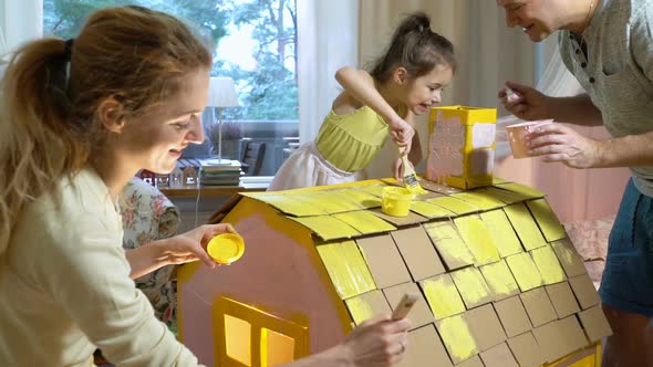 Young Family with Child Building and Painting Toy Cardboard House Together.