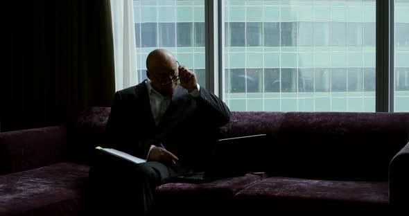 Tired Businessman Is Working with Papers and Laptop, Sitting on Couch in Office Room