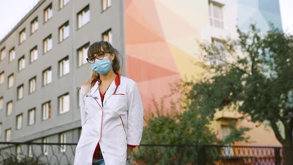Portrait of Shy Female Doctor or Nurse in Surgical Mask and White Medical Gown Looking at You