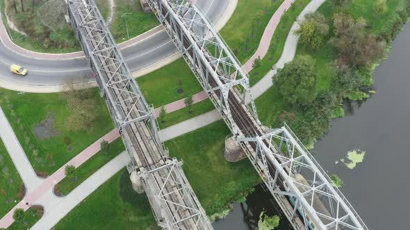 Electric train passes through the railway bridge across the river. Aerial view.