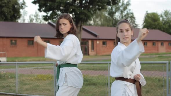 Two Young Girls in White Kimonos Demonstrate Standard Fighting Karate Stances While Standing on the