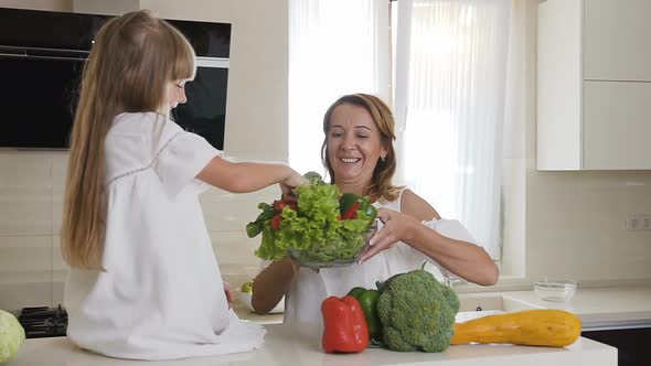 A Cute Girl with Long Hair in White Dress Takes a Tomato from a Glass Plate