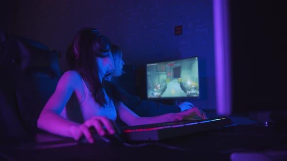 Two Pretty Gamer Girls Playing an Online Game in the Dark Neon Gaming Club