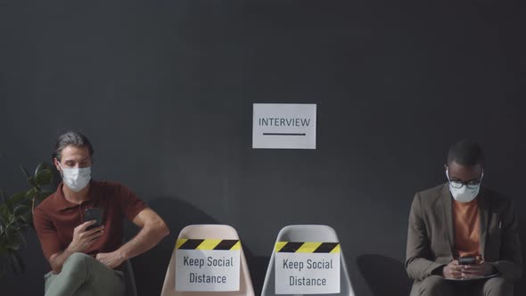 Two Men in Masks Messaging on Smartphones and Waiting for Job Interview