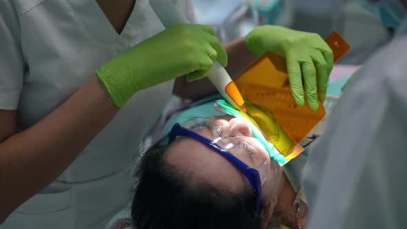 High Angle View of Caucasian Woman in Dental Chair with Unrecognizable Doctor and Nurse Using UV