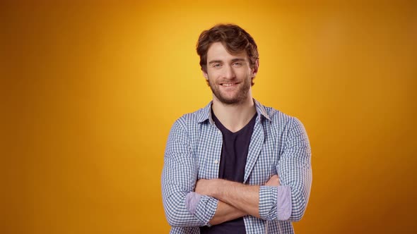 Young Beared Guy in Casual Shirt Nods Approvingly Against Yellow Studio Background