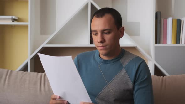 Sad Man Sitting on Couch at Home Reads Received Bad News 