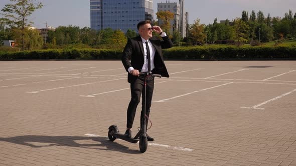 A Young Businessman Stands with an Electric Scooter in the City on a Sunny Day