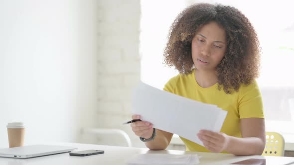 African Woman Reading Documents while Sitting in Office