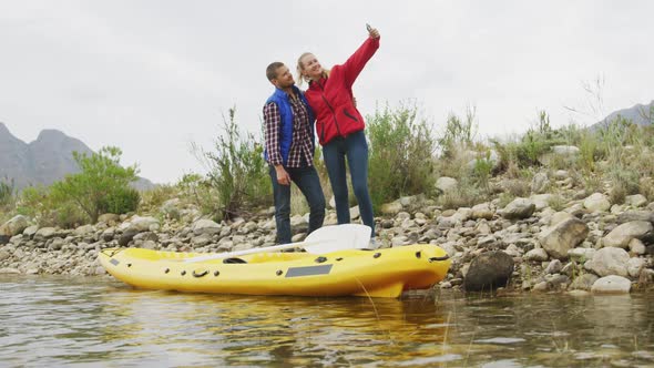 Caucasian couple having a good time on a trip to the mountains, standing next to a kayak, taking a s