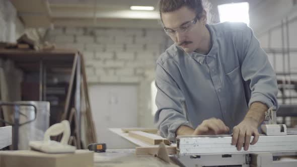 Caucasian Carpenter Positioning and Cutting Piece of Wood on Table Saw