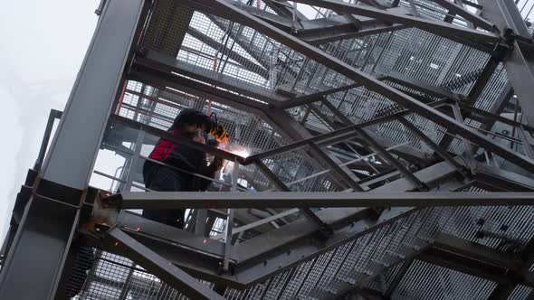 A welder performs repair work on a metal structure at a factory