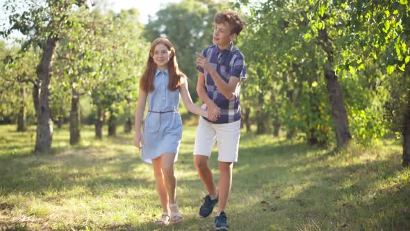 Wide Shot Portrait of Redhead Teenage Couple Holding Hands Strolling in Sunrays in Spring Summer